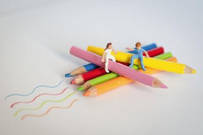 Zwei Miniaturfiguren sitzen auf bunten Stiften