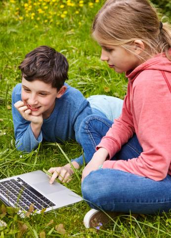Ein Junge und ein Mädchen sitzen im Gras an einem Laptop