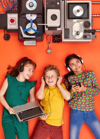 Drei Kinder mit Kopfhörern liegen auf dem Boden und hören Musik