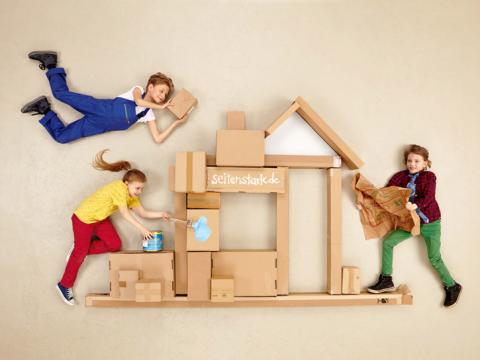 Drei Kinder bauen zusammen ein Haus aus Pappkartons