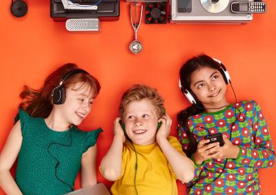 Drei Kinder mit Kopfhörern liegen auf dem Boden und hören Musik