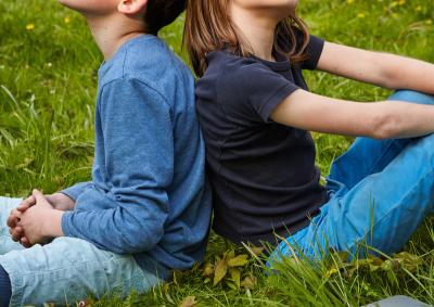 2 Jungen sitzen Rücken an Rücken im Gras und überlegen